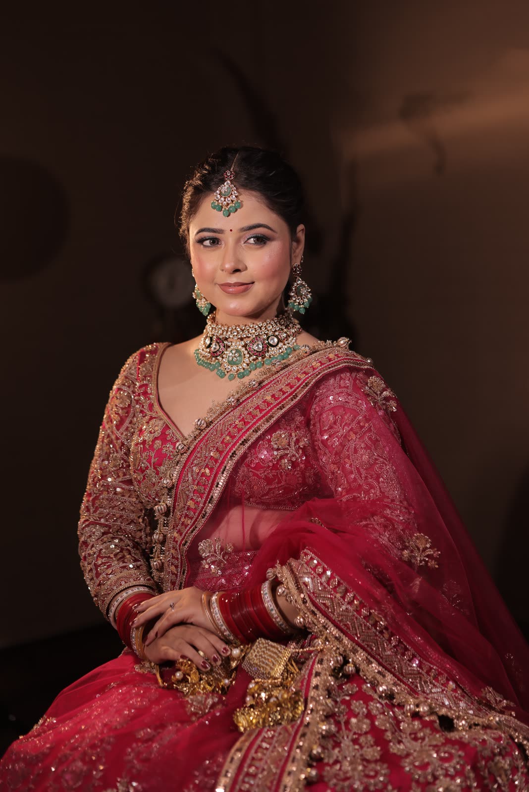 Bride in a red embroidered lehenga with green polki jewellery